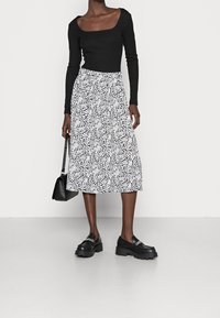 Top lungo a maniche nere a coste abbinato a una gonna bianca lunghezza ginocchio con un motivo floreale nero. Mocassini neri spessi e una borsa piccola.