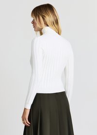 Col roulé blanc côtelé avec manches longues et taille ajustée, associé à une jupe plissée foncée. Texture lisse, design minimaliste.