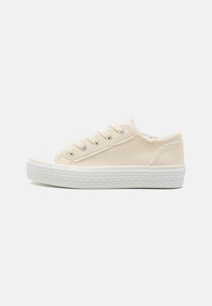 Beige lerret low-top sneakers med hvit gummitå og teksturert såle. Inkluderer fem snøringer og en myk innvendig fôr.
