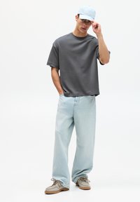 Casquette de baseball bleu clair, t-shirt gris oversize et jeans droits en denim clair. Chaussures beiges avec semelles marron. Look simple et décontracté.