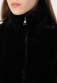 Schwarze Kunstfelljacke mit hohem Kragen und Reißverschluss. Sie verfügt über eine glatte, weiche Textur und silberne Hardware-Akzente am Reißverschluss.
