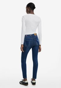 Haut à manches longues blanc associé à un jean slim bleu foncé avec des accents floraux brodés sur la ceinture arrière et des baskets noires.