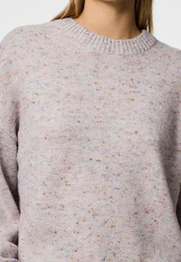 Mujer vistiendo un suéter de punto de color púrpura claro con manchas de colores y un cuello redondo acanalado.