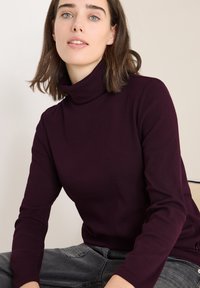 Burgundowy, prążkowany golf z długimi rękawami, w połączeniu z ciemnoszarymi dżinsami. Materiał wydaje się być miękki i lekko teksturowany.