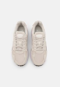 Beige athletic shoes made of mesh and suede, featuring a rounded toe, lace-up design, and a textured rubber sole.