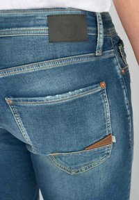 Blauwe denim jeans met een licht vervaagde textuur, voorzien van een bruine leren label op de achterste tailleband en twee achterzakken met stikdetails.