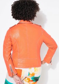Orangefarbene Lederjacke mit figurbetontem Design, Schulterakzenten und Reißverschlussdetails an den Ärmeln, ausgestattet mit glatter Textur und sichtbaren Nahtlinien.