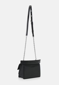 Sac à main en cuir noir présentant un design structuré, une bandoulière en cuir réglable et des accents en chaîne. L'avant comporte un détail de logo en relief.