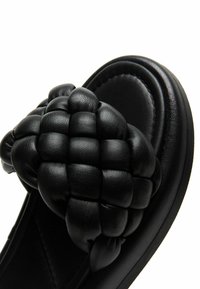 Sort slidesandal med tyk polstret sål og overdimensioneret vævet læderrem over toppen.