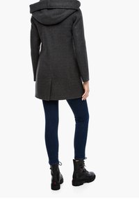 Grijze wolblend jas met een capuchon, middellange snit, zijzakken, gecombineerd met donkerblauwe jeans en zwarte veterschoenen tot de enkel.