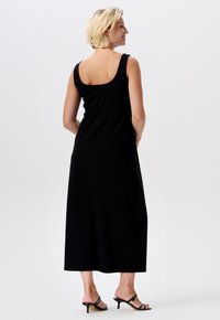 Schwarzes Maxikleid mit breiten Trägern, taillierter Passform und glatter Baumwollstruktur. Die Rückansicht zeigt einen runden Ausschnitt und einen knöchellangen Saum.