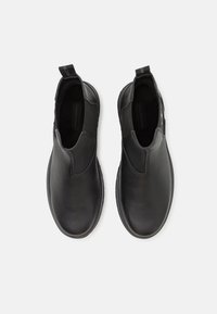 Zwarte instap-schoenen met een leren bovenwerk met structuur, elastische zijkanten en een trekloopje bij de hiel. Platte rubberen zool met minimale profiel.