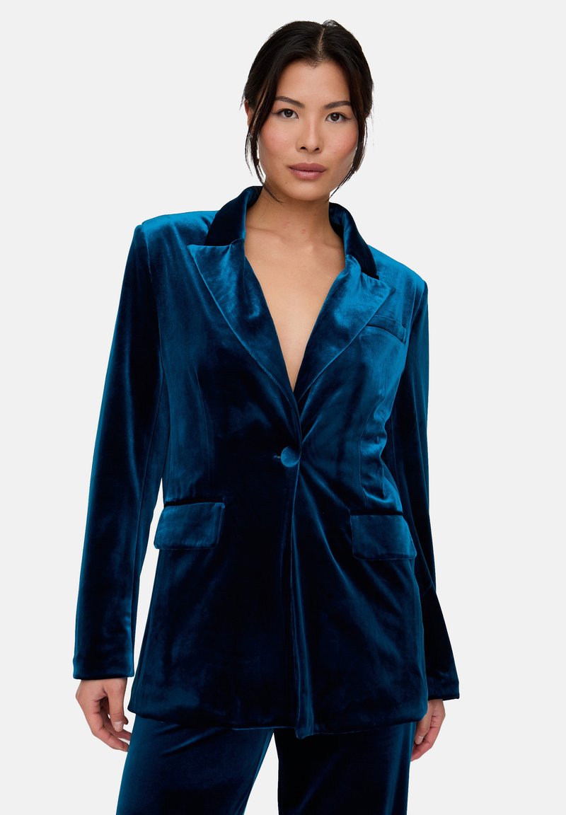 Samtblazer in tiefem Petrol mit Reverskragen, einreihiger Knopfleiste und Vordertaschen. Glatte Textur und taillierte Passform.