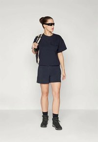 Navy short-sleeve shirt with pocket, matching shorts, black sunglasses, and black hiking boots. Carrying a beige and black-striped backpack.