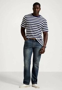 Marineblå og hvit stripet t-skjorte med korte ermer, kombinert med mørkeblå jeans og hvite joggesko, som fremhever et avslappet, klassisk utseende.