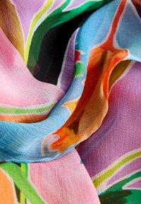 Tissu doux et multicolore avec des motifs floraux abstraits, comprenant des nuances de rose, bleu, vert, orange et noir, drapé en plis lisses.