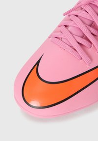 Nike focicipő sima rózsaszín felsőrésszel, narancs színű logóval fekete kerettel, és texturált fűzőkkel a biztos illeszkedésért.