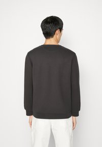 Mörkgrå sweatshirt med långa ärmar, rund hals och ribbade mudd. Slät tygtextur, minimalistisk design, bärs med vita byxor.