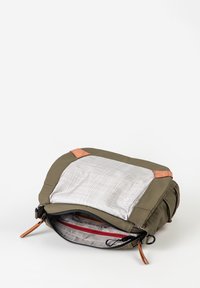 Borsa verde oliva con chiusura a cerniera; presenta una fodera a motivo a griglia e dettagli in pelle marrone chiaro negli angoli. L'interno include una tasca con zip rossa.