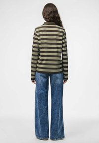 Gestreepte lange mouwen top in donkerbruin met groene en witte strepen, gecombineerd met wijde denimjeans. Zachte stof met een relaxte pasvorm.
