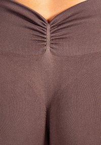 Leggings marron côtelés avec une taille froncée, présentant un motif texturé. Le tissu semble doux et extensible.