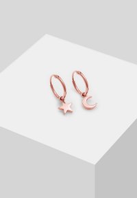 Orecchini a cerchio in oro rosa con un charm a forma di stella e mezzaluna, texture liscia, design minimalista e forma rotonda. Ogni charm pende dal cerchio.