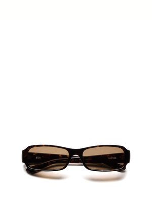 Lunettes de soleil rectangulaires en écaille de tortue avec des verres teintés brun foncé et une monture épaisse reposant sur une surface blanche.