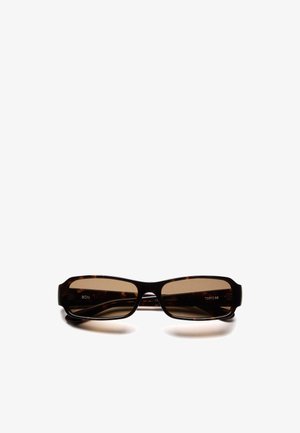 Lunettes de soleil rectangulaires en écaille de tortue avec des verres teintés brun foncé et une monture épaisse reposant sur une surface blanche.