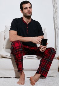 Heren zwart kortemouw pyjama-top met rode geruite accenten, gecombineerd met rode geruite broek. Zachte stof, ontspannen pasvorm, geen zichtbare patronen op het top.