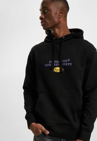 Felpa nera con tasca frontale, con testo viola "JACK & JONES NINETEEN NINETY" e emblema giallo. Tessuto morbido e strutturato.
