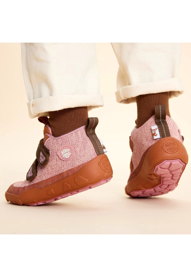 Pink knit sneakers with brown rubber soles, featuring adjustable straps, a logo patch, and a textured design.