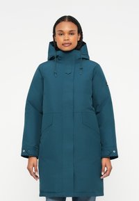 Casaco impermeável em teal com colarinho alto, capuz ajustável, dois bolsos frontais e punhos com botão de pressão. Textura suave e design minimalista.