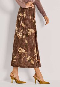 Een bruine fluwelen rok met bloemenpatroon, geplooid ontwerp en een lengte tot halverwege de kuit. Gepaard met gele slingback hakken en een lichte trui.
