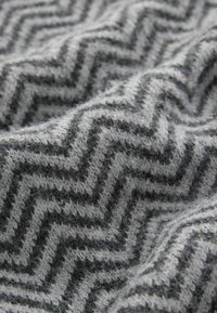 Gewebe mit einem Zickzackmuster in Grau und Dunkelgrau. Weiche Textur mit leichter Fusselbildung, die seine Wärme und Tiefe unterstreicht.