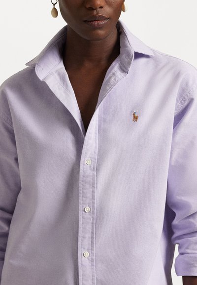 Light purple button-up shirt made of soft fabric, featuring a slight sheen, a pointed collar, and a small embroidered logo on the chest.