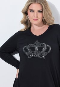 Czarna koszula z długim rękawem, ozdobiona srebrną koroną z cyrkonii z przodu i dekoltem w serek. Gładki materiał o luźnym kroju.