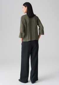 Top verde oliva, texture con maniche 3/4 e orlo arrotondato, abbinato a pantaloni neri larghi. Design semplice, senza motivi o decorazioni visibili.