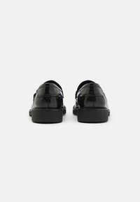 Paire de chaussures habillées en cuir noir brillant vues de dos sur un fond clair uni.
