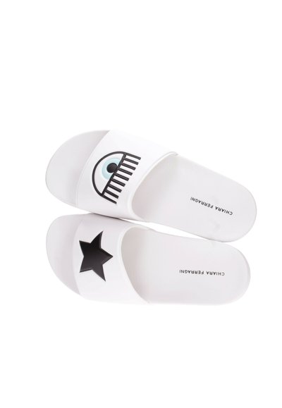 Chanclas blancas con gráficos de ojo negro y estrellas en las correas; textura suave y suela plana. Logo en el lateral.
