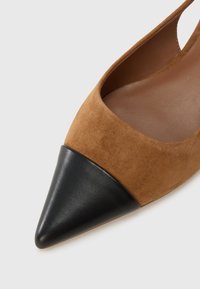 Καφέ σουέντ πεδιλάκι με ιμάντα στο πίσω μέρος, μυτερό μύτη και αντίθετη μαύρη δερμάτινη άκρη. Ο σχεδιασμός περιλαμβάνει μια εσοχή στο πλάι για καλύτερο αε ρισμό.