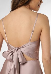 Vestito di un leggero lavanda con sottili spalline, schiena scoperta e un grande fiocco annodato in vita, realizzato in un materiale liscio e simile al raso.