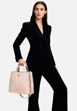 Borsa tote rosa trapuntata con borchie dorate e logo, dotata di manici corti e tracolla staccabile, mostrata con un completo nero.