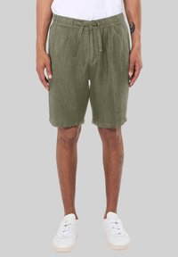 Olivgrüne Leinen-Shorts mit elastischem Bund und Kordelzug, ausgestattet mit seitlichen Taschen und einem lockeren Schnitt. Getragen mit weißen Sneakers.
