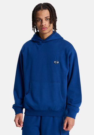 Niebieska bluza z kapturem wykonana z miękkiej mieszanki bawełny, wyposażona w przednią kieszeń i małe logo na piersi. Luźny krój z ściągaczami na mankietach i u dołu.