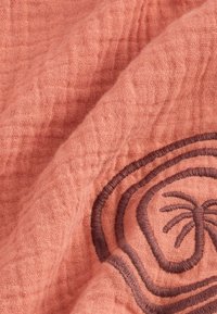 Peachfarvet tekstureret stof med brune broderede palmetrædesign, der har krøllede mønstre og en blød, åndbar væv.