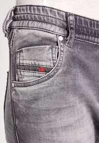 Szare dżinsy z lekkim przetarciem i przednią kieszenią z czerwonym logo, z metalowym zapięciem na guzik oraz przeszyciami.