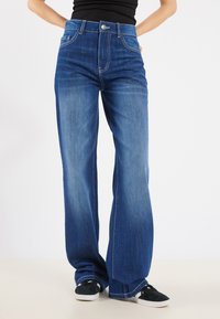 Jean en denim bleu à jambe large et taille haute, avec une fermeture à un bouton à l'avant, des coutures décoratives et une texture douce.