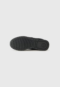 Schwarze Gummisohle eines Sneakers mit einer strukturierten, gemusterten Lauffläche, die Rillen und kreisförmige Akzente aufweist. Glatte Kanten und minimales Branding.