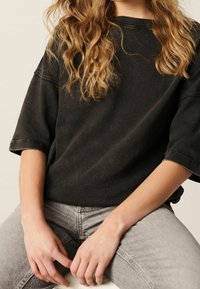 Black oversized t-shirt with a soft texture and short sleeves, paired with light grey jeans. Simple design with no prominent patterns or accents.