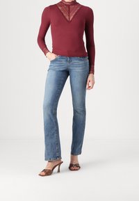 Burgundy långärmad topp med spetsdetaljer vid halsringningen, tillsammans med ljusblå utsvängda jeans och bruna högklackade sandaler med nitar.